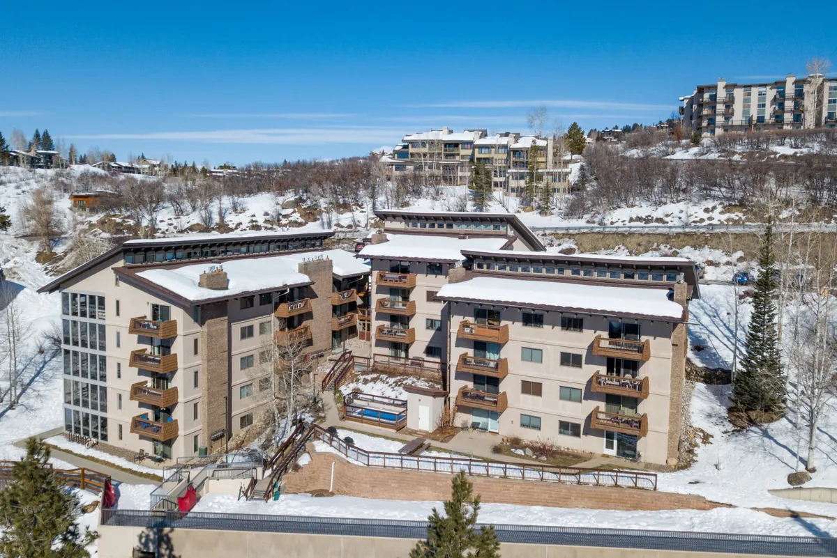 This image captures the exterior of the property with snow-covered rooftops, balconies, and surrounding trees set against nearby hills. The cozy, tranquil setting highlights the building's proximity to winter activities and scenic vistas, suggesting easy access to local amenities and outdoor adventures.