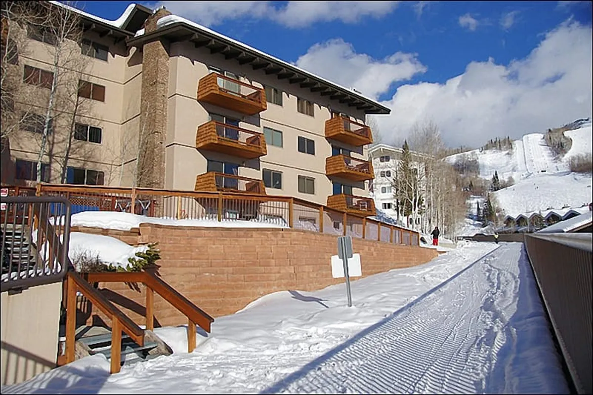 A cozy, multi-level building with wooden balconies, surrounded by a pristine snow-covered ground. The inviting exterior hints at warm gatherings, après-ski festivities, and the comfort of returning to a welcoming home base after a day of adventure.