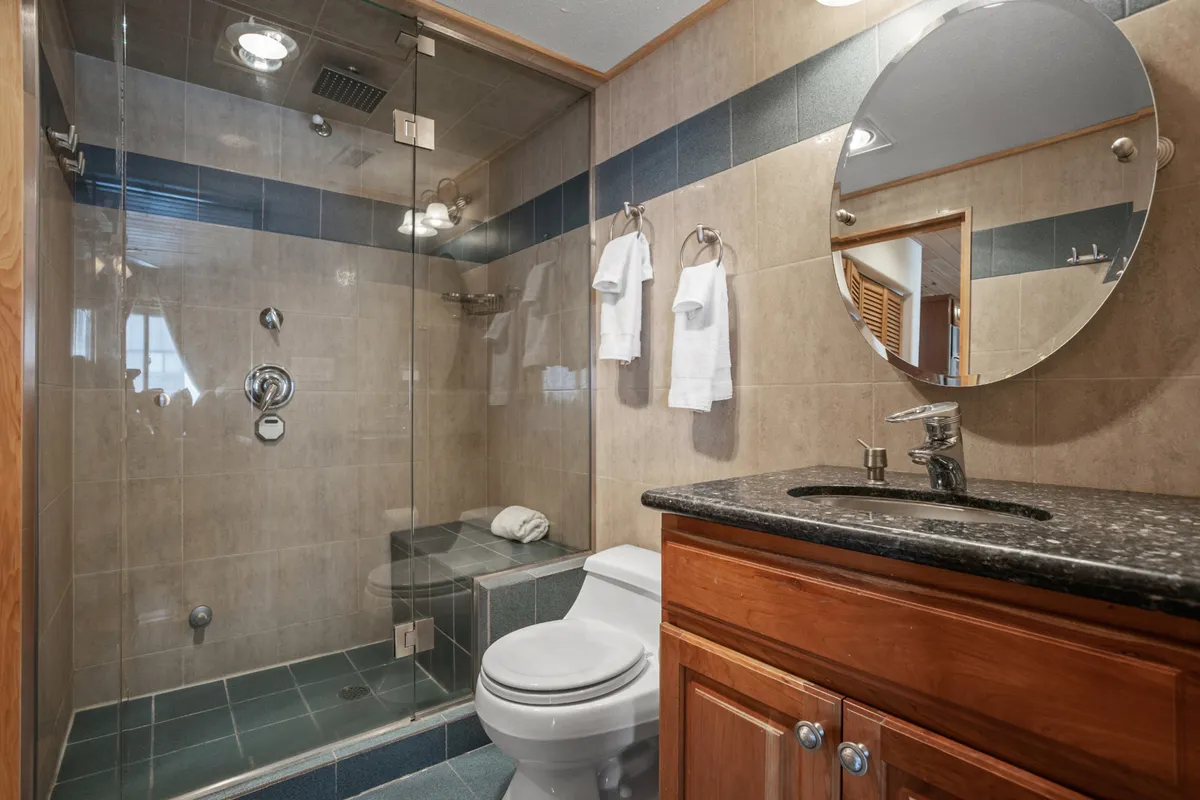 A spa-inspired bathroom featuring a glass shower enclosure, round mirror, wooden cabinetry, and plush white towels. The clean lines and serene color palette create an atmosphere of wellness and relaxation.