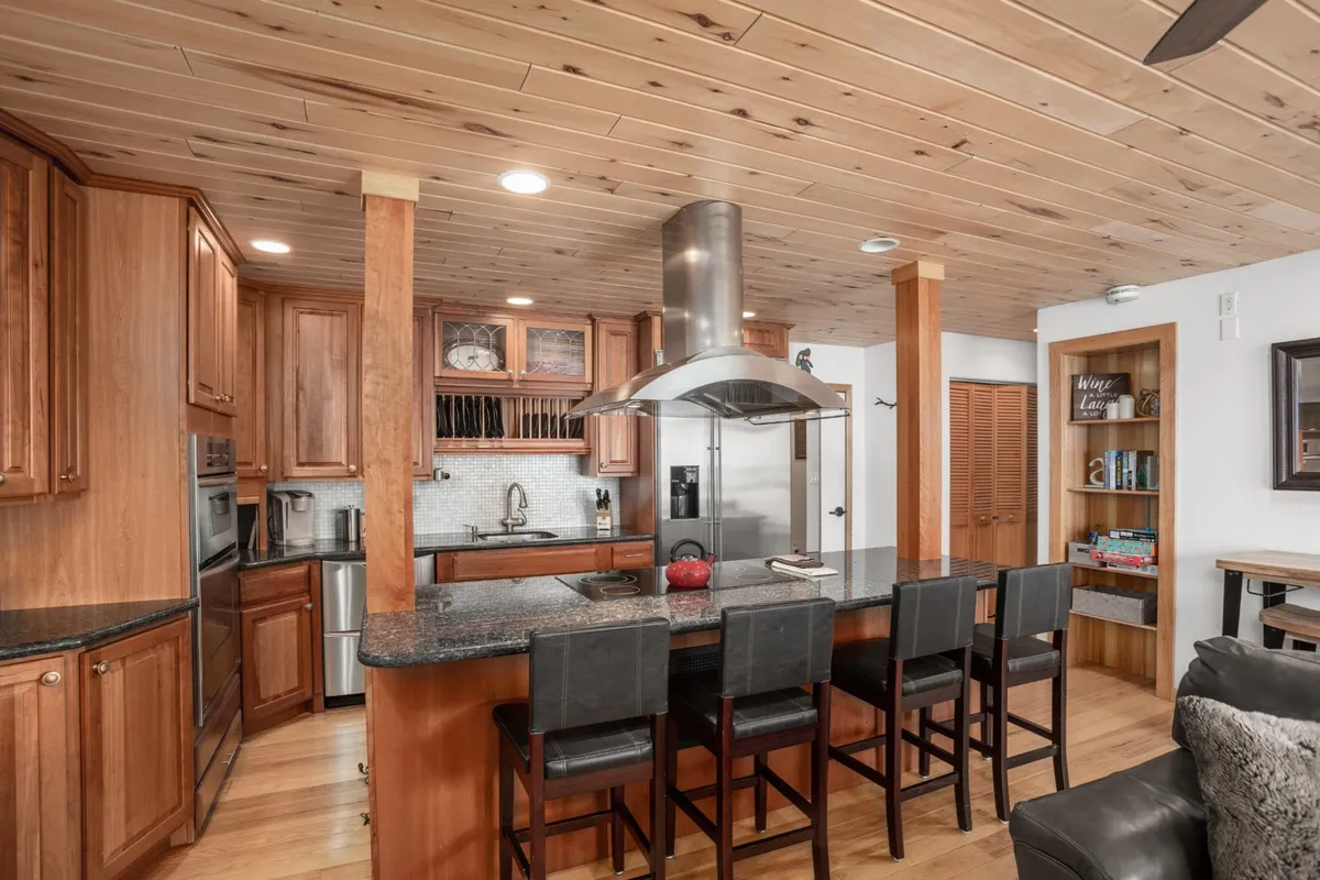 A welcoming kitchen interior features a kitchen island, stainless steel hood, wood cabinets, and black countertops—emphasizing comfort and functionality for meal preparation.