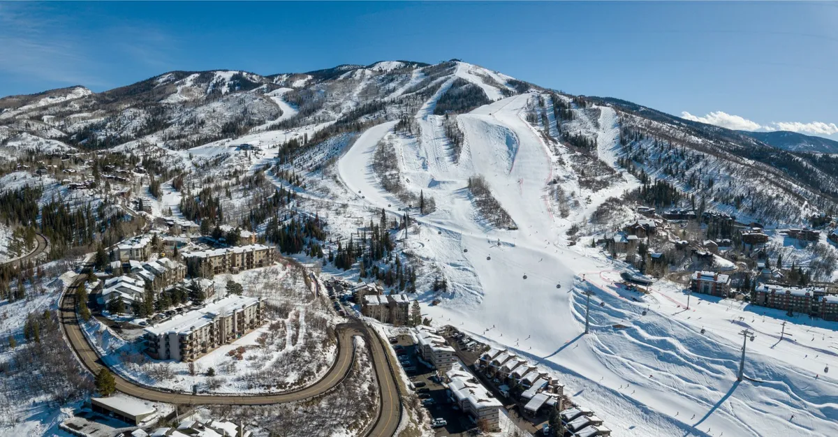 A breathtaking winter scene showcasing snow-covered slopes dotted with skiers and snowboarders, ski lifts in action, and nearby residential buildings nestled at the foot of the mountain. The environment exudes both excitement and tranquility, perfectly capturing the thrill of ski-in/walk-out access.